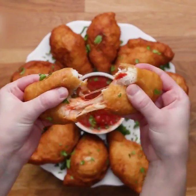 two hands holding a plate with fried food on it and dipping sauce in the middle