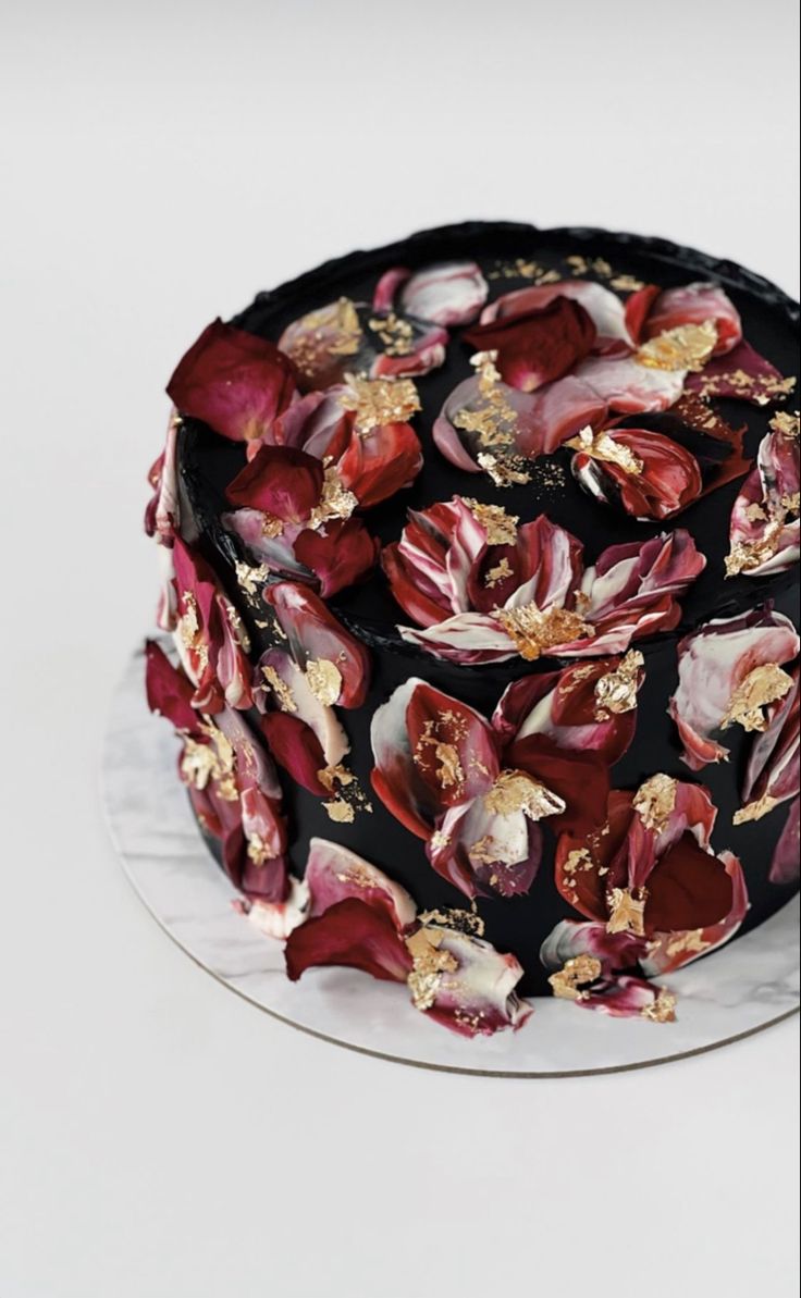 a chocolate cake with red and gold flowers on it's icing, sitting on a white plate