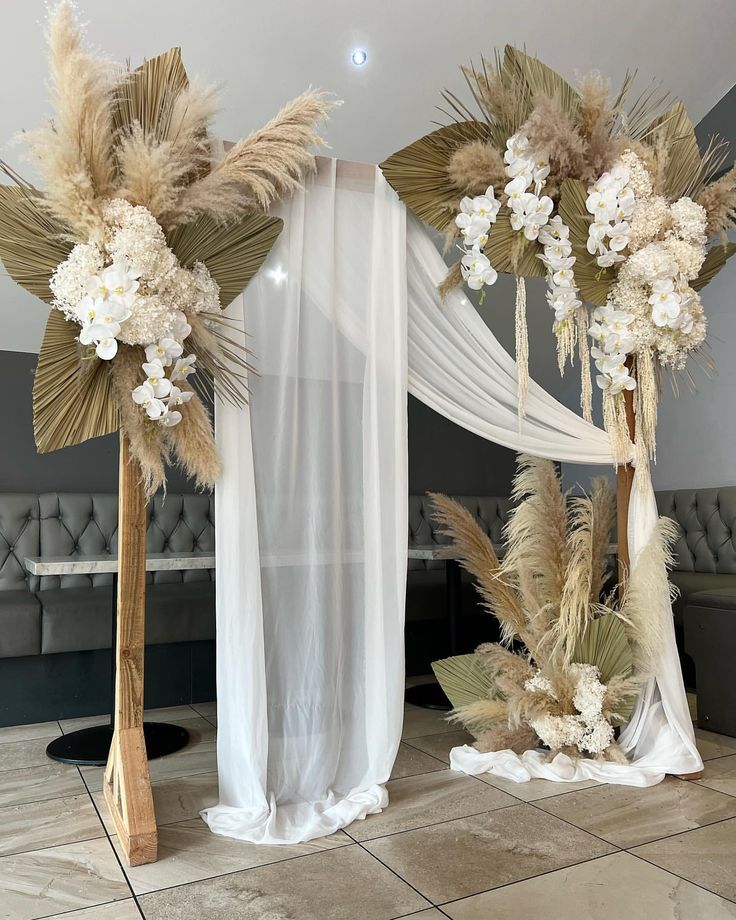 two white and gold wedding archs decorated with flowers, pamodia and feathers