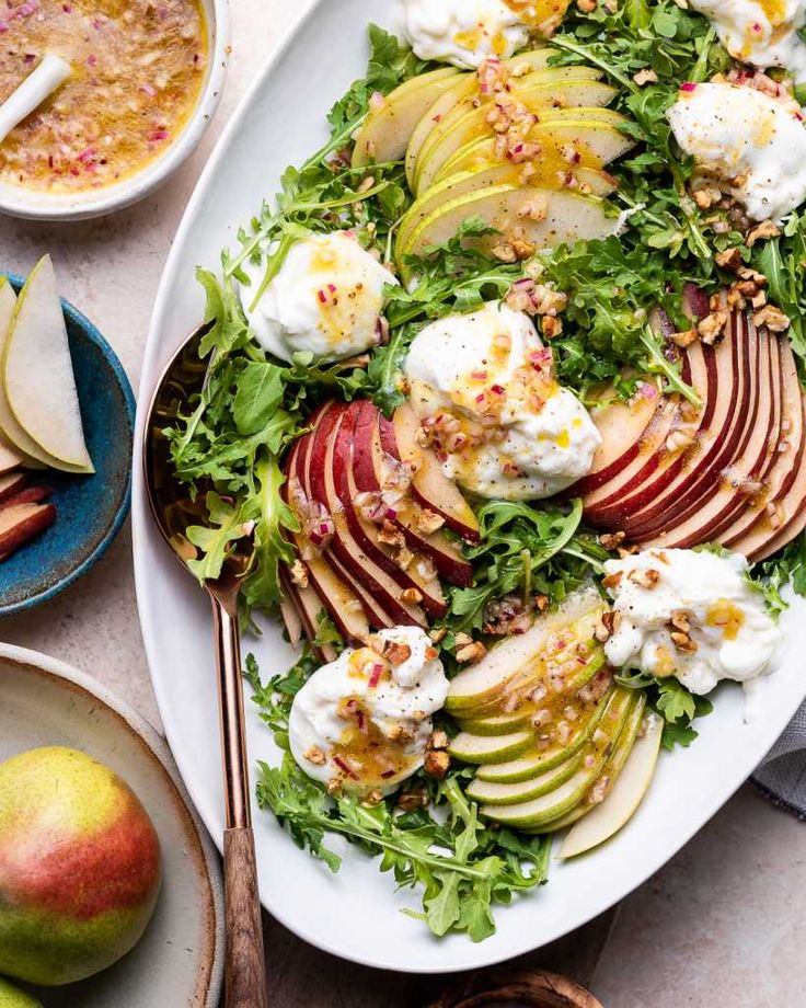 a white plate topped with an apple salad next to bowls of fruit and dips