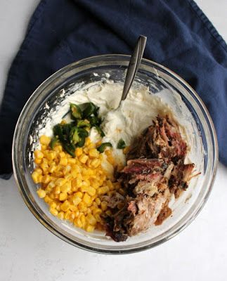 a glass bowl filled with meat, corn and mashed potatoes on top of a blue napkin