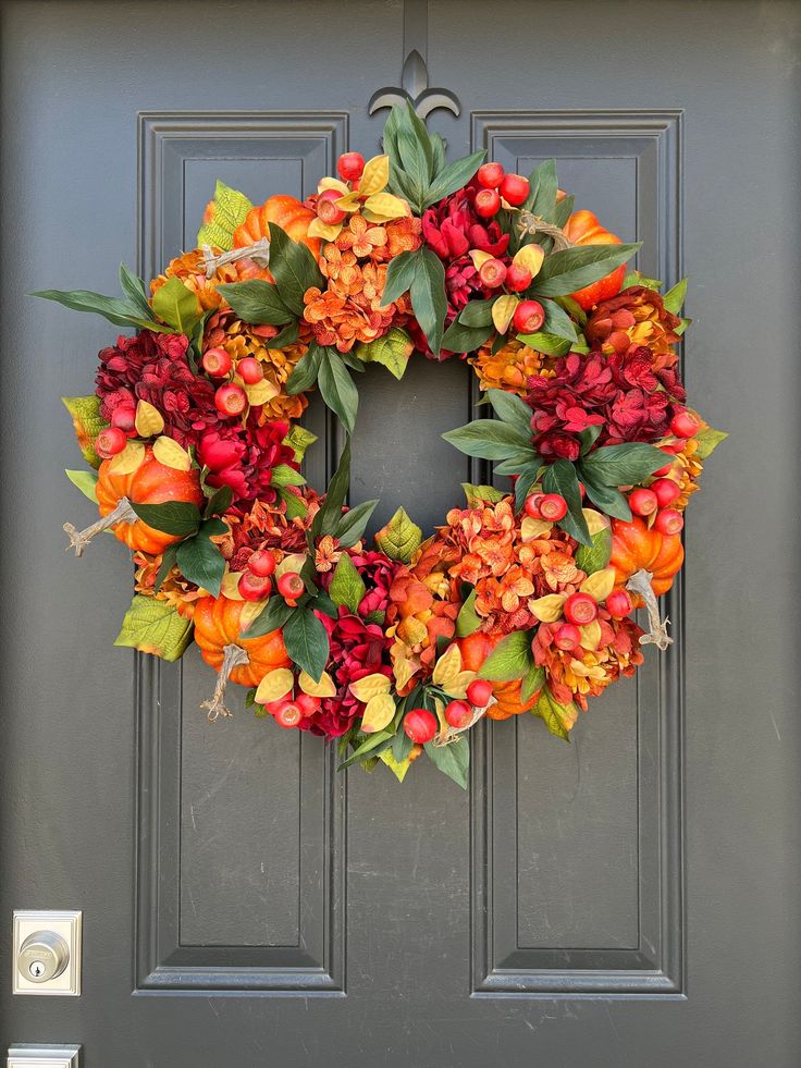 a wreath with pumpkins and flowers on the front door