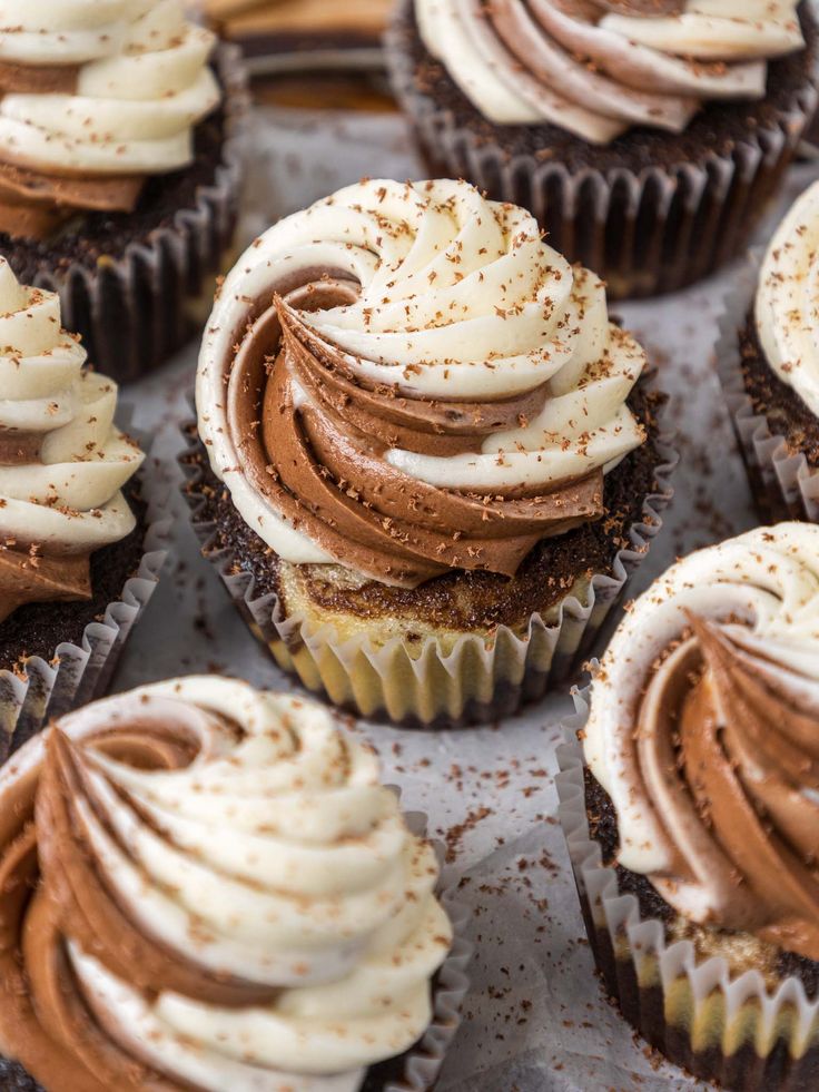 chocolate cupcakes with white frosting and sprinkles sitting on a baking sheet