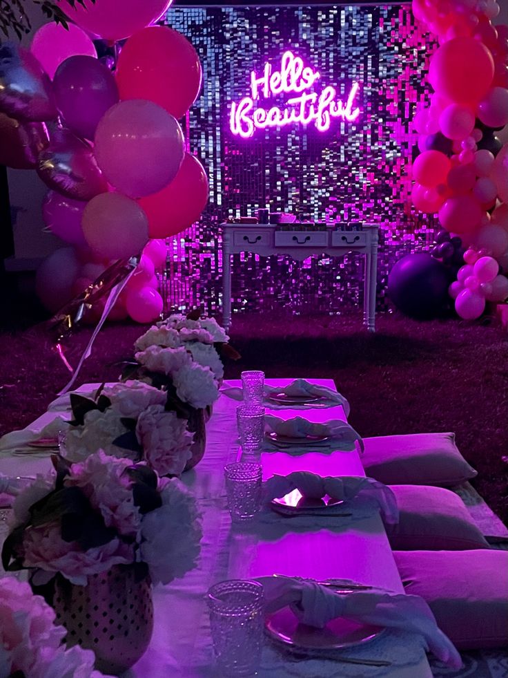 a table set up for a party with pink and purple balloons on the wall behind it