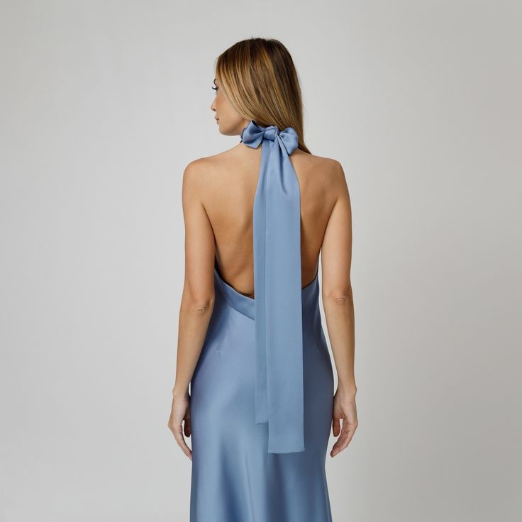 A captivating blend of elegance and allure, our Skye Open Back Halter Dress exudes undeniable charm. Tailored with a flattering bias cut from blue double silk satin, it drapes gracefully over the silhouette. The halter neckline delicately frames the shoulders, while the revealing back adds a note of sensuality. For a playful and feminine look, you can transform the silk tie neck into a chic bow, or you can let it drape loosely, adding a touch of laid-back sophistication to your ensemble.  Wear it with flats for an effortlessly refined look or dress it up with a precious pair of heels. Each Il Volo item is handmade by skilful artisans in our Bucharest atelier and it is created in limited series. 100% Italian Double Silk Satin.  Gentle dry clean. Do not wash. Do not use chlorine based bleach Elegant Tie Back Satin Dress For Evening, Blue Evening Dress With Satin Finish For Weddings, Blue Satin Finish Evening Dress For Wedding, Blue Slip Dress For Gala, Formal Backless Bias-cut Silk Dress, Blue Satin Slip Dress For Gala, Elegant Satin Tie-back Dress For Gala, Elegant Satin Dress With Tie Back For Gala, Blue Satin Finish Evening Dress For Formal Occasions