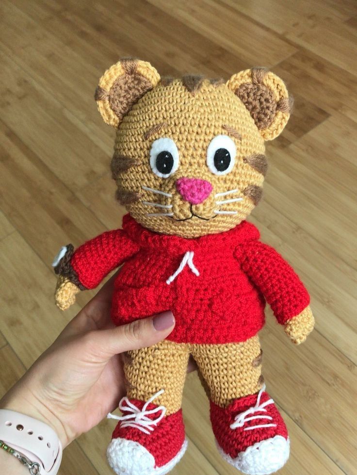 a crocheted tiger doll is being held by someone's hand on a wooden floor