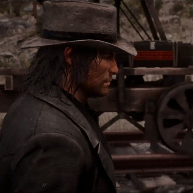 a man with long hair wearing a fedora and standing in front of a machine