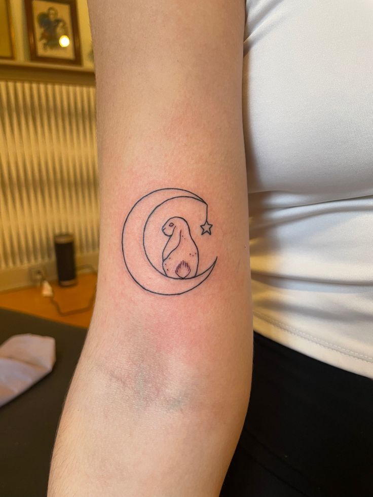 a woman's arm with a small tattoo of a dog sleeping on the moon