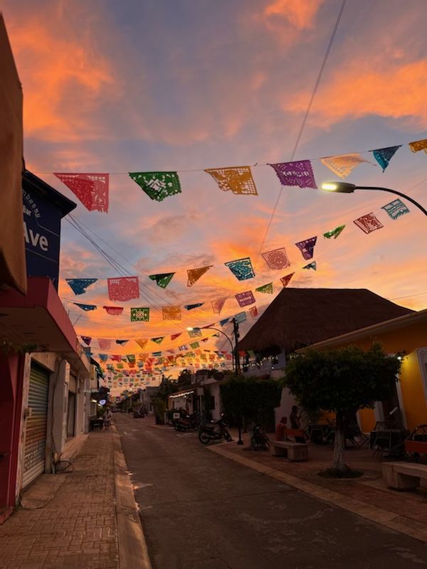 the sun is setting and there are many colorful flags strung from the buildings on the street