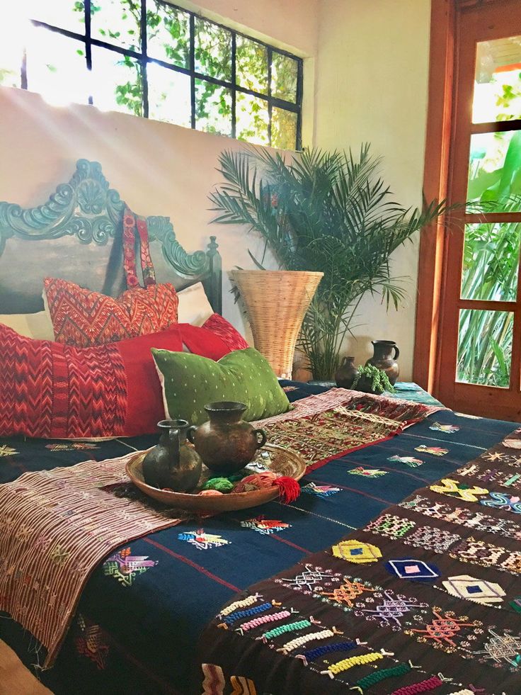 a bed covered in pillows and blankets next to a potted plant on top of it