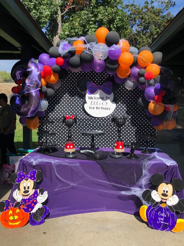 mickey and minnie mouse balloons on display at an outdoor event with purple table cloths