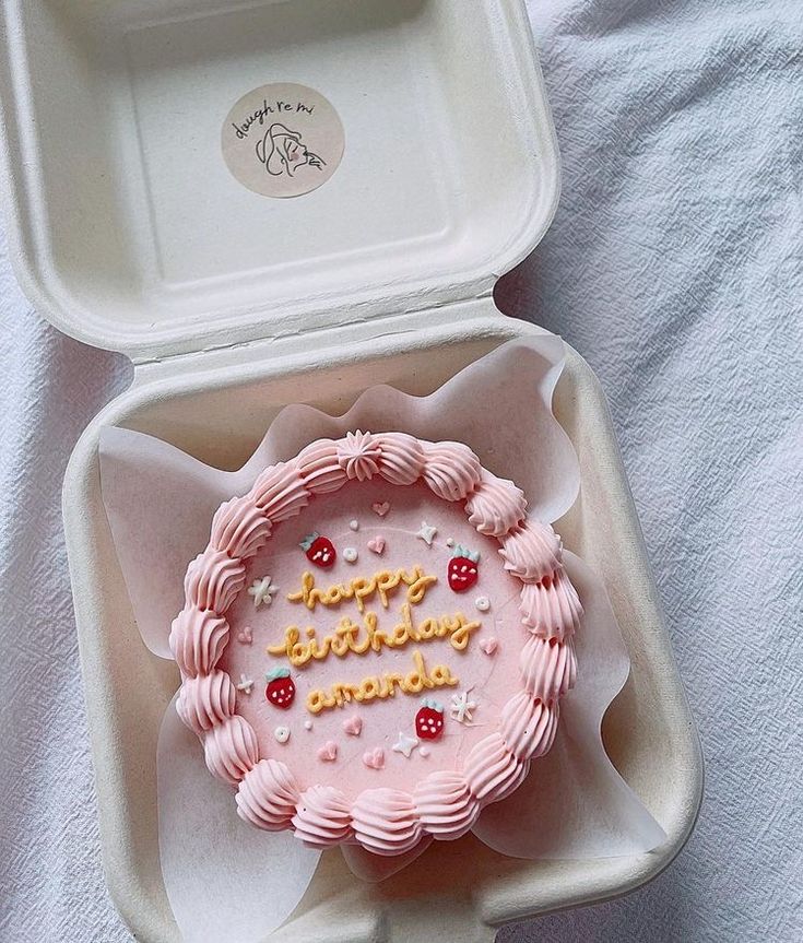 a pink birthday cake in a white box on a bed with the words happy birthday written on it