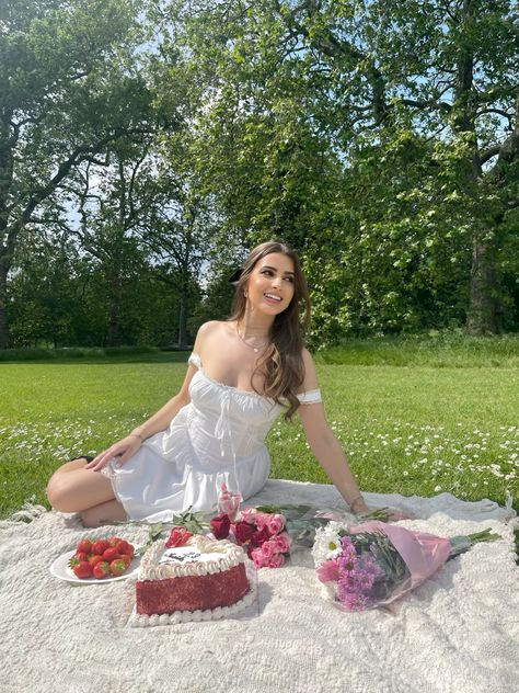 a woman sitting in the grass with some cake and strawberries