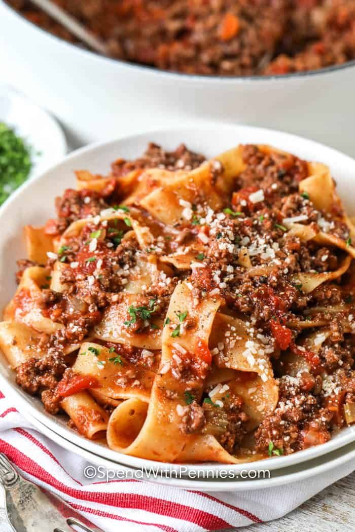 a white bowl filled with pasta and meat sauce on top of a red and white striped napkin