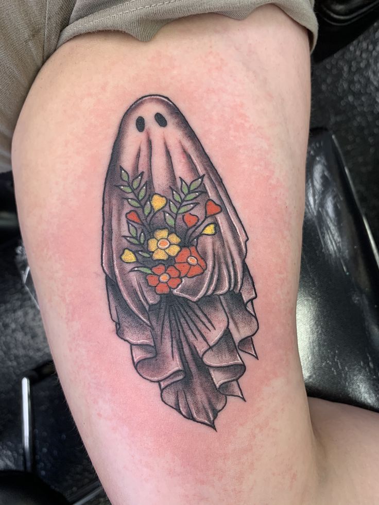 a woman's thigh with a ghost and flowers tattoo design on it, sitting next to a black chair