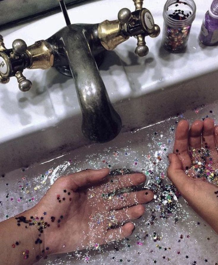 two hands are sprinkled with glitter in front of a sink faucet