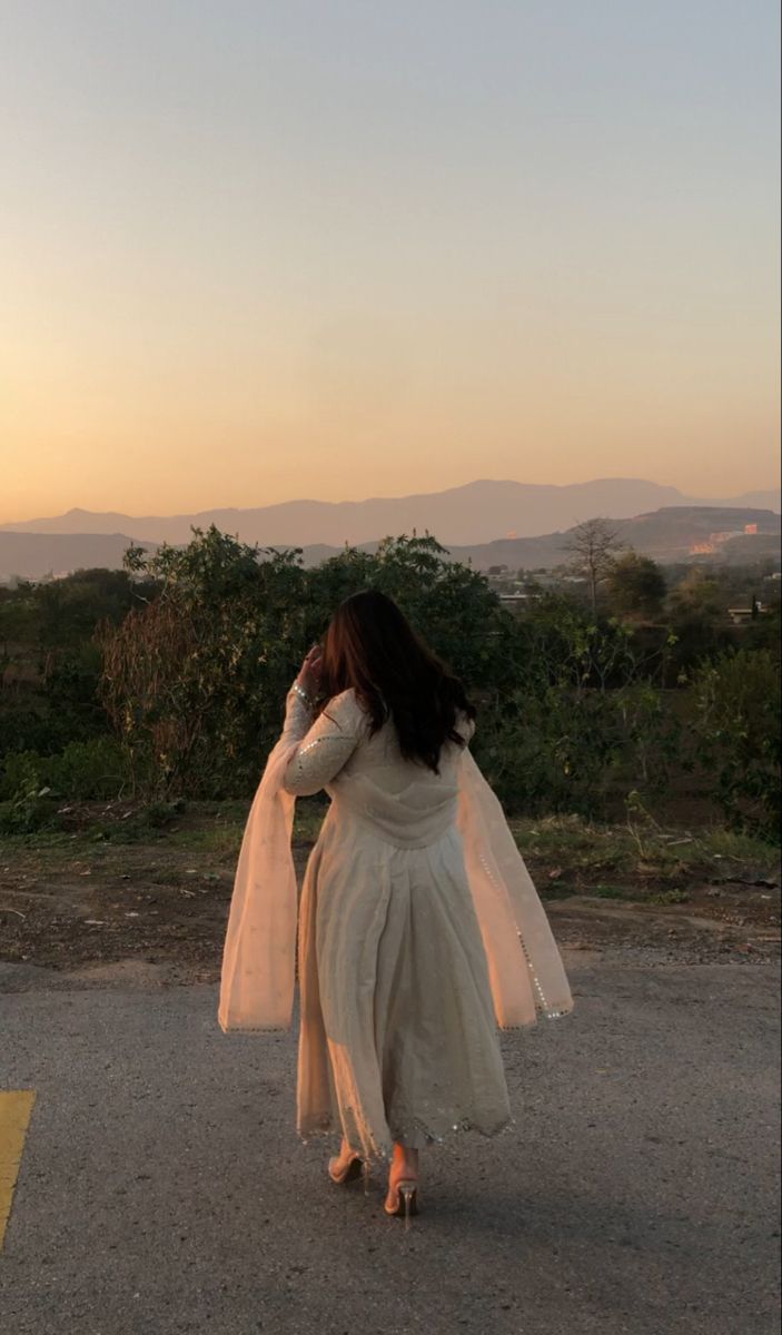 a woman in a white dress is walking down the road