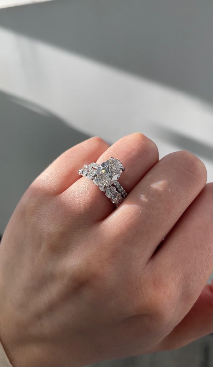 a woman's hand with a diamond ring on top of her finger, in front of a window