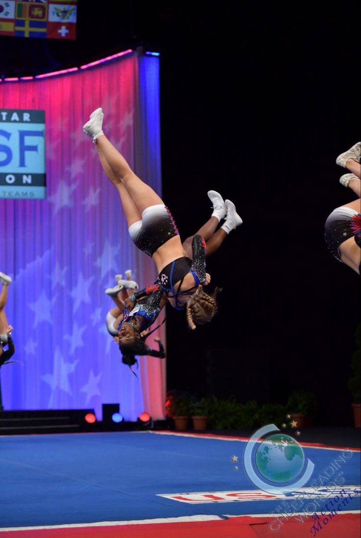 two female cheerleaders performing in front of an american flag on the sidelines