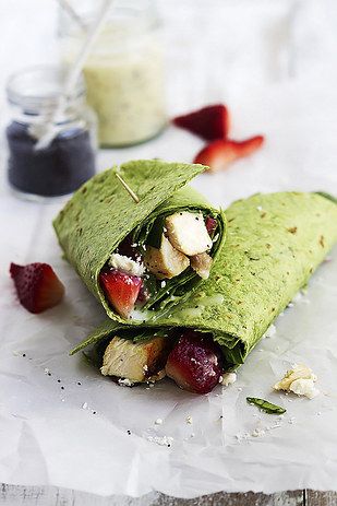 a wrap filled with fruit and cheese on top of white paper next to strawberries