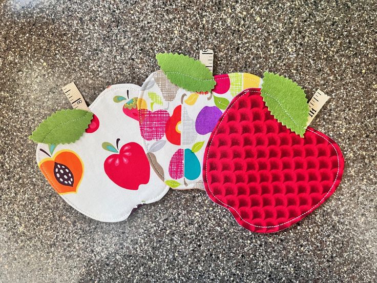 three pieces of cloth with apples on them sitting on a counter top next to each other