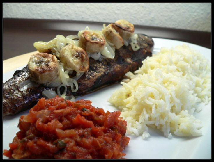 a white plate topped with meat covered in sauce and rice next to other food items