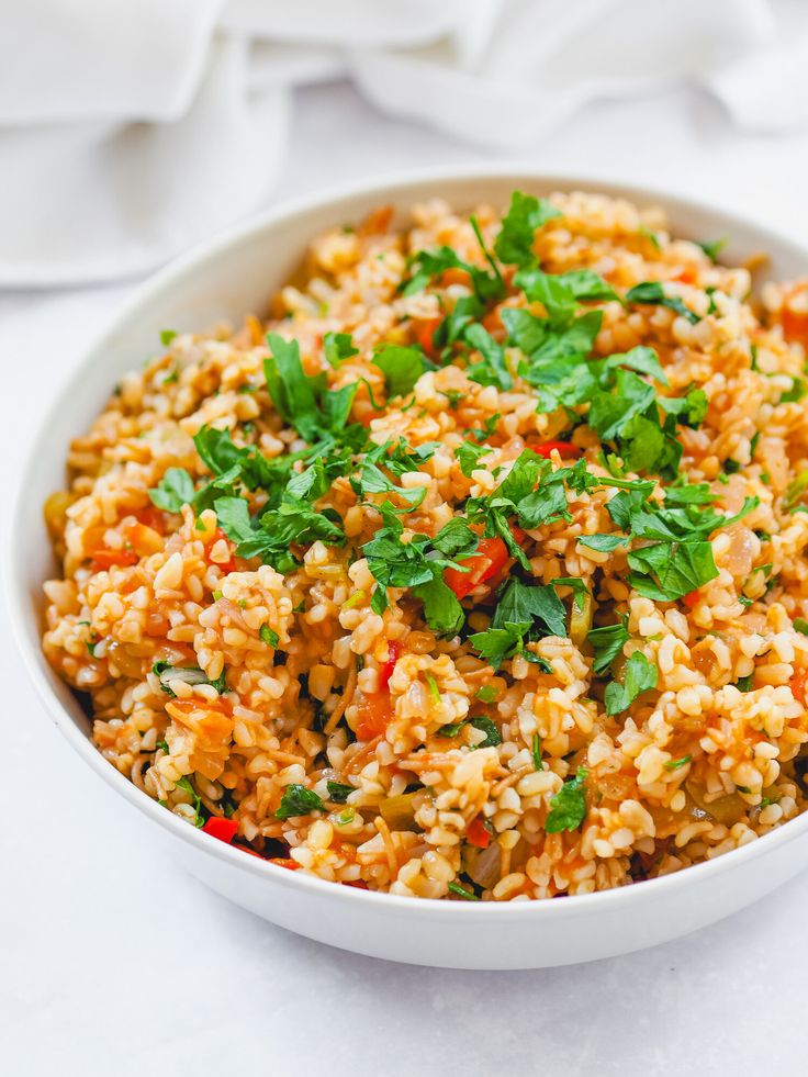 a white bowl filled with rice and veggies on top of a table next to napkins