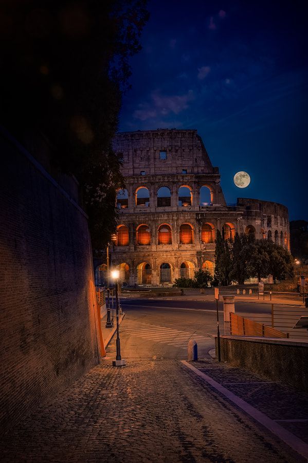 an old building lit up at night with the moon in the sky