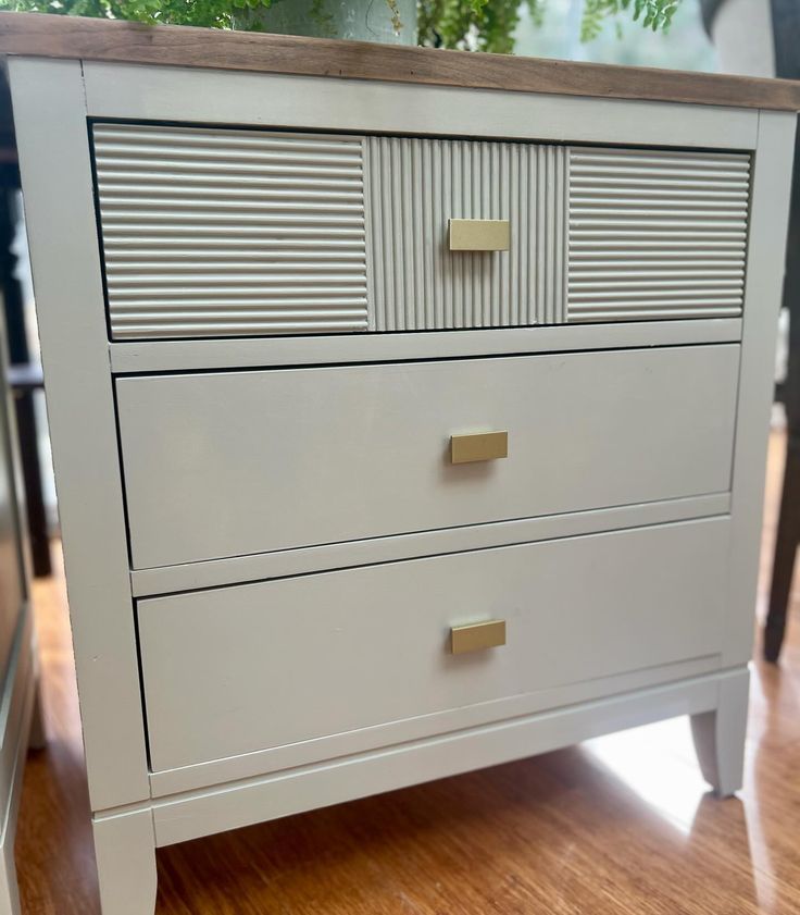 a white dresser sitting on top of a hard wood floor next to a planter