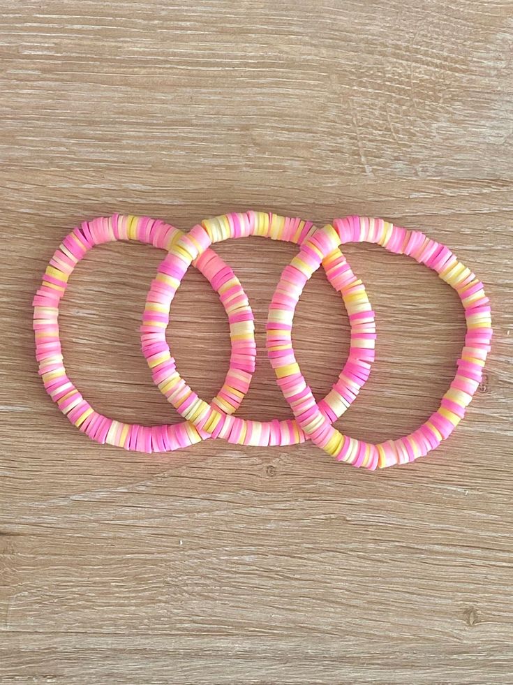 three pink and yellow bracelets sitting on top of a wooden table