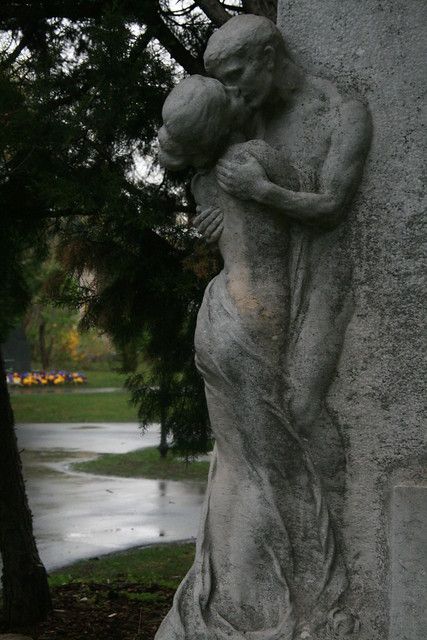 the statue is leaning up against the wall in front of the tree and grass area