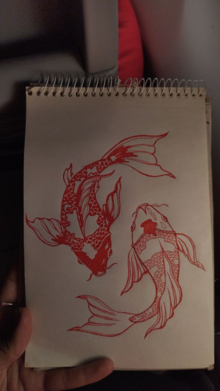 a drawing of two fish in red ink on white paper, held up by someone's hand