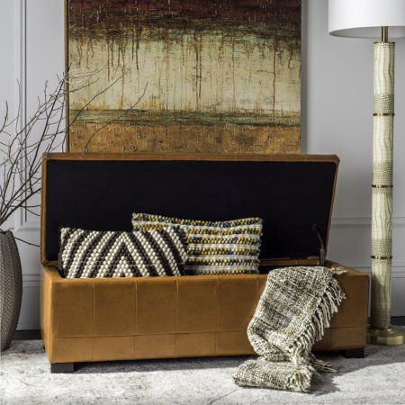 a brown leather bench with pillows on it in front of a painting and floor lamp