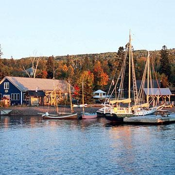 several boats are docked in the water near some houses and trees with fall colors on them