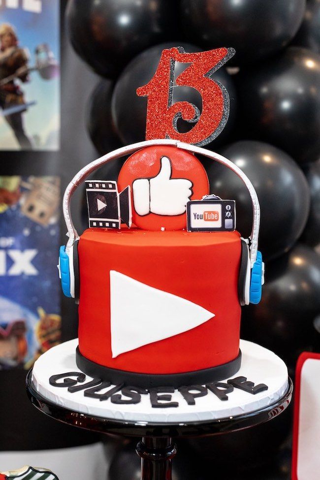 a red and black birthday cake with headphones on it's top is surrounded by balloons