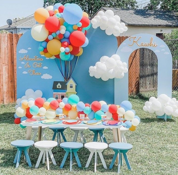 an outdoor birthday party with balloons on the table and blue arch in the back ground