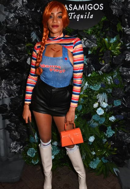 a woman with red hair wearing overalls and holding an orange purse in front of a wall