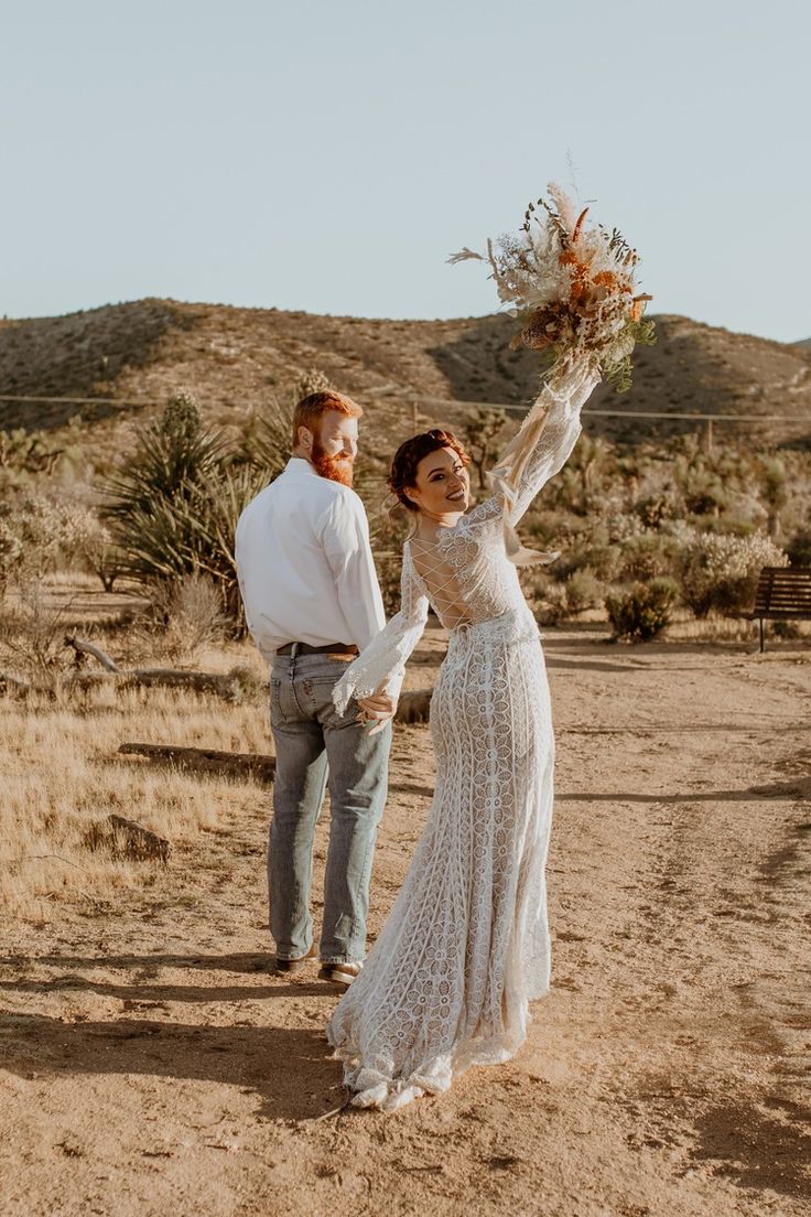 a man and woman are walking in the desert holding bouquets with their hands up