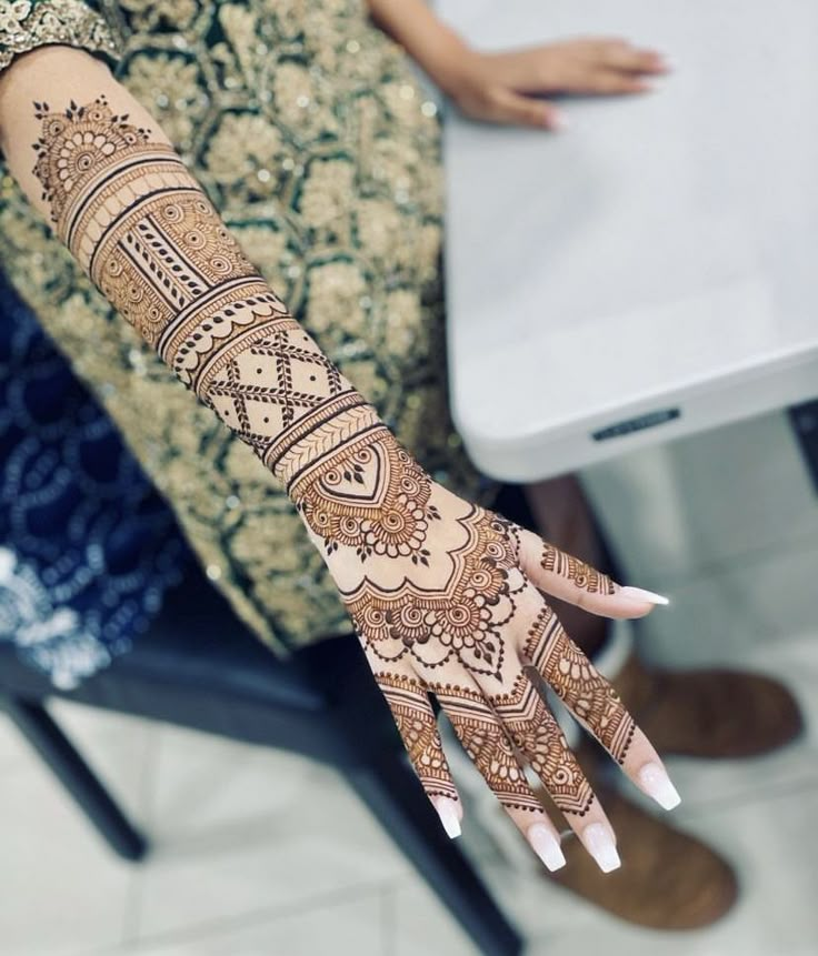 a woman's hand with henna tattoos on her left arm and wrist, sitting in front of a laptop computer