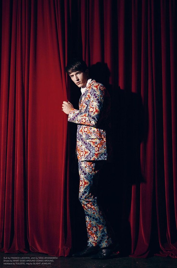 a man standing in front of a red curtain with his hands on his chest and arms crossed