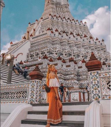 a woman standing in front of a white and gold building with stairs leading up to it