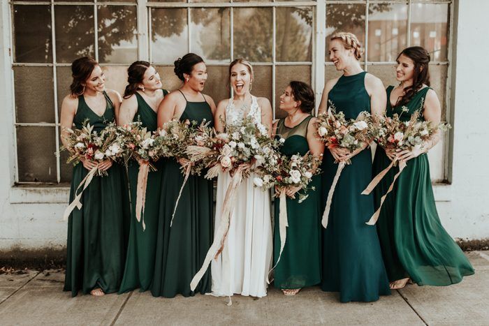 a group of women standing next to each other in front of a window holding bouquets