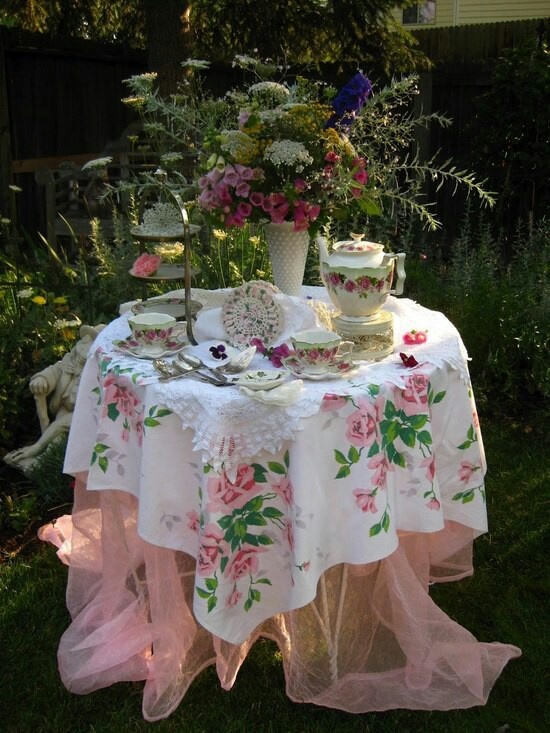 a table that has some tea on it in the grass with flowers and plants around it