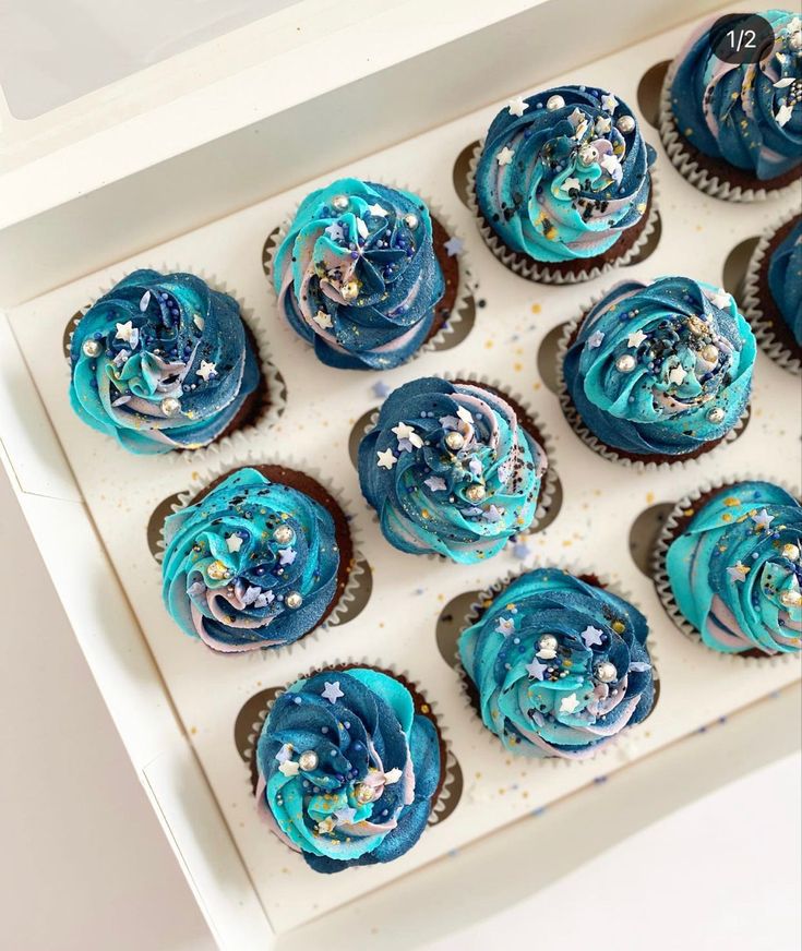 twelve cupcakes with blue frosting and sprinkles in a white box