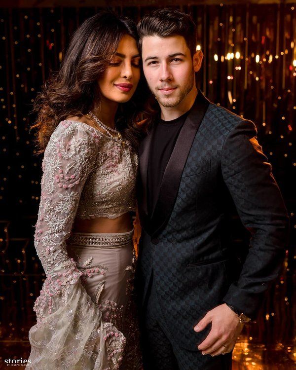 two people standing next to each other in front of a gold wall with lights behind them