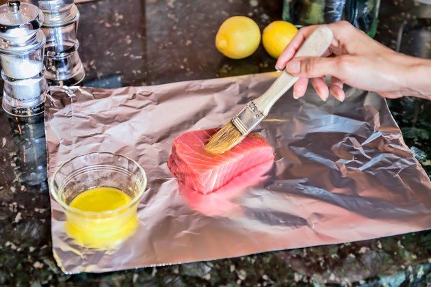 someone using a brush to paint the salmon on aluminum foil with lemons in the background