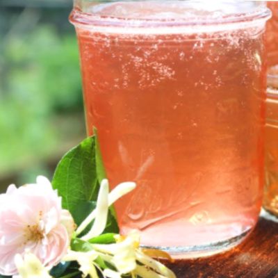 two jars filled with liquid sitting on top of a wooden table next to pink flowers