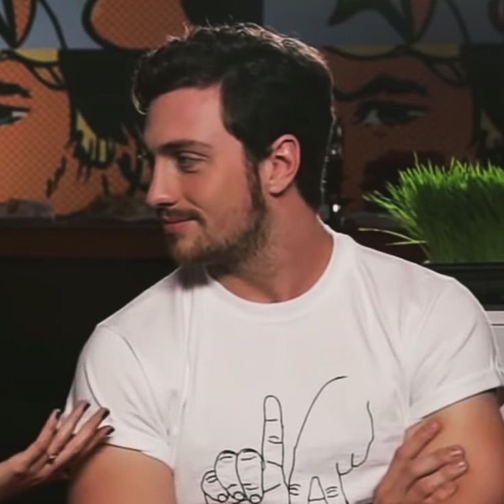 a man in a white t - shirt sitting down with his hands on his chest