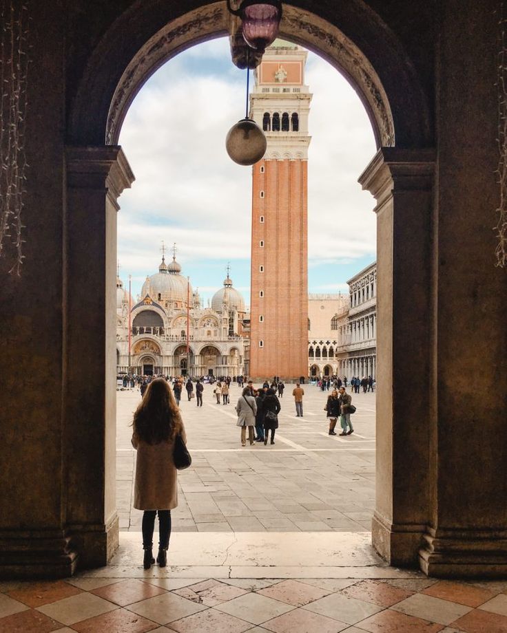 a woman is standing in an archway looking at the clock tower that stands behind her