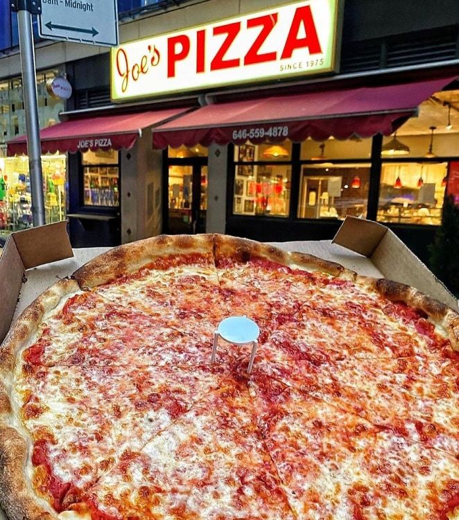 a large pizza sitting on top of a cardboard box in front of a storefront